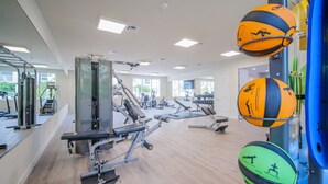 Un gimnasio con equipo de ejercicio, espejos y ventanas amplias.