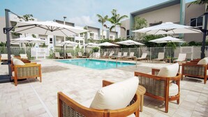 Un área junto a la piscina con sillones de descanso y sombrillas, piscina y un edificio al fondo.