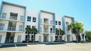 Un hotel de varios pisos con balcones, palmeras y un estacionamiento.