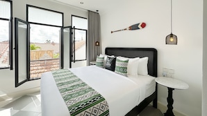 Habitación de hotel con una cama grande, una mesita de noche, una lámpara colgante y vistas de la ciudad a través de las ventanas.