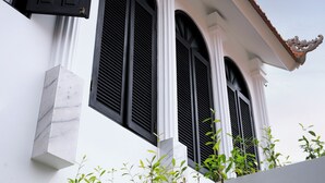 Un edificio con tres grandes ventanales con contraventanas negras, columnas blancas y un techo de tejas.