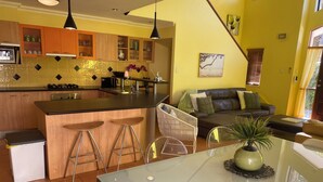 A modern kitchen with a central island, bar stools, and a dining table with a glass top. - Aloha home-Amazing location for all GC has to offer amazing home for the family. (Labrador)