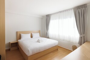Una cama bien hecha con sábanas blancas, cabecera de madera y mesita de noche.