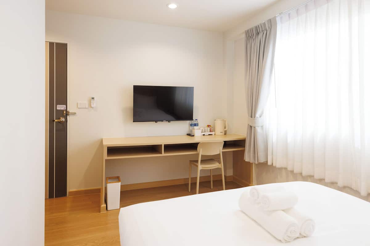A hotel room with a bed, a desk, a chair, a television, and a window with curtains.