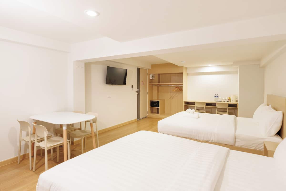 A hotel room with two beds, a desk, a chair, and a TV on the wall.