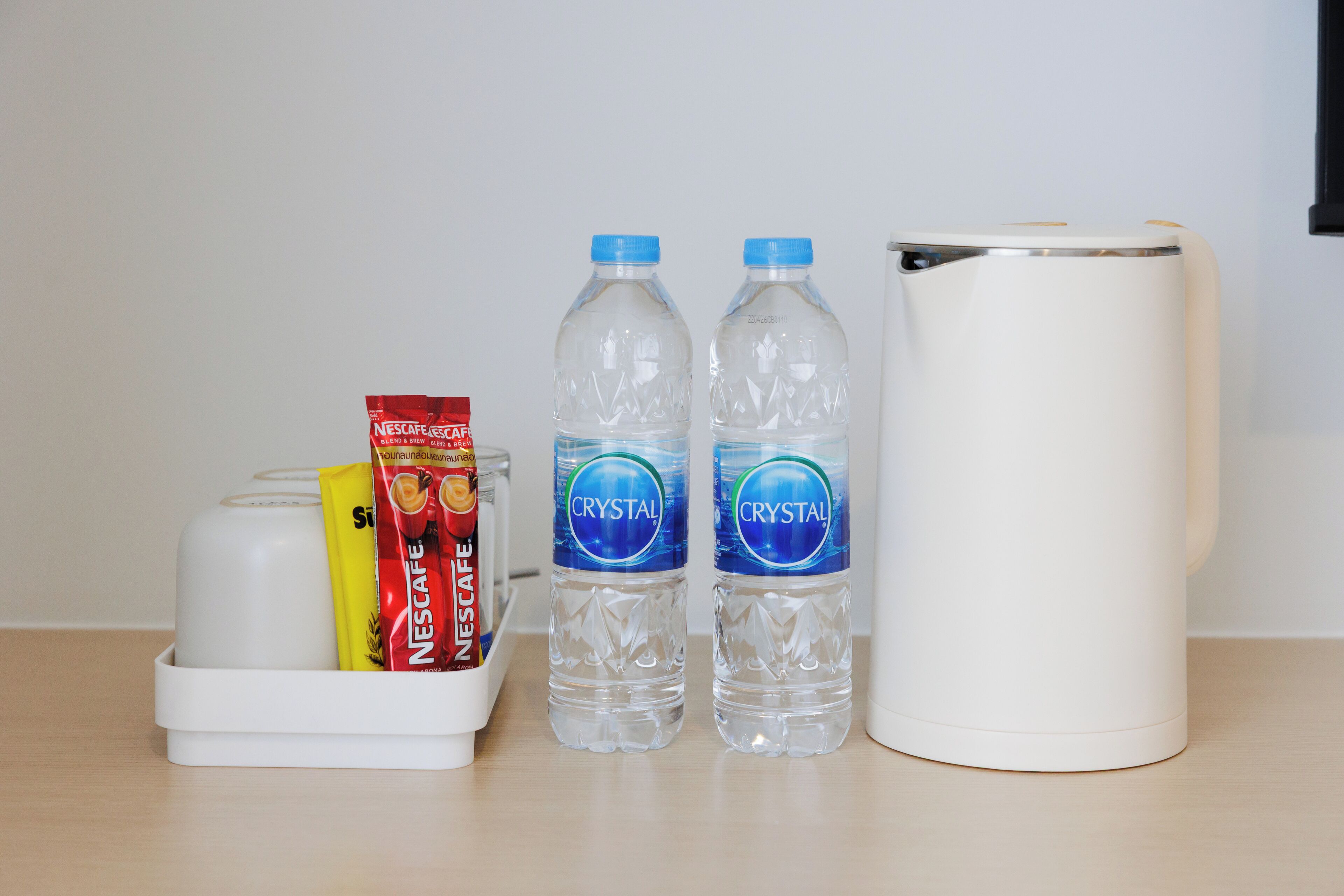 A white coffee maker, two water bottles, and a coffee pod holder with Nescafe and Crystal coffee pods.