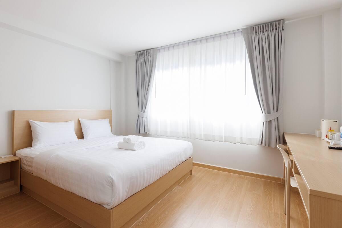 A hotel room with a bed, a desk, and a window with curtains.