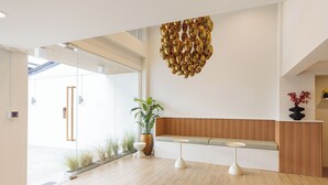 A modern reception area with a wooden bench, two white tables, and a decorative gold chandelier.