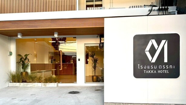 The exterior of Takka Hotel with a modern design, including a reception area with glass doors and potted plants.
