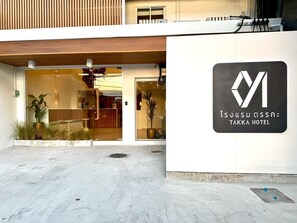 The exterior of Takka Hotel with a modern design, including a reception area with glass doors and potted plants. - Takka Hotel - Bearing (Bangkok)