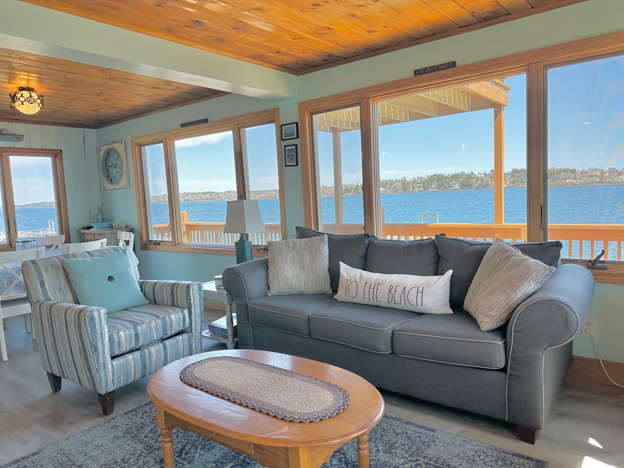 A cozy living room with a view of the water, featuring a sofa, armchair, and a wooden coffee table.
