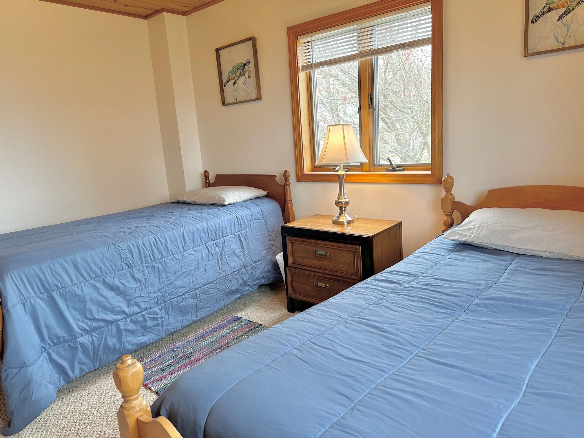 A bedroom with two single beds, a nightstand with a lamp, a wooden headboard, and a window with blinds.