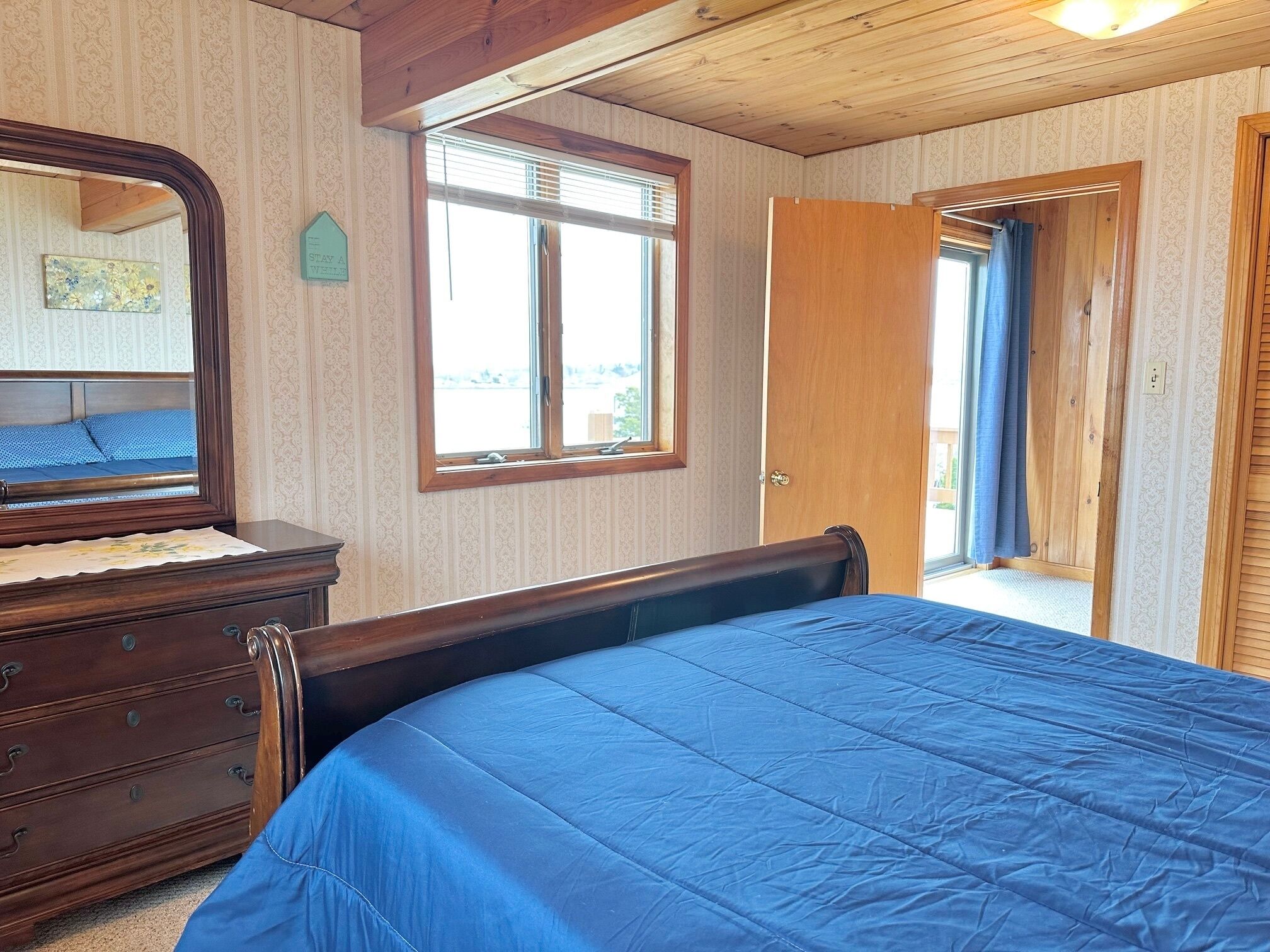 Una camera da letto con un letto di legno, una cassettiera, una finestra e una porta che dà su uno spazio esterno.