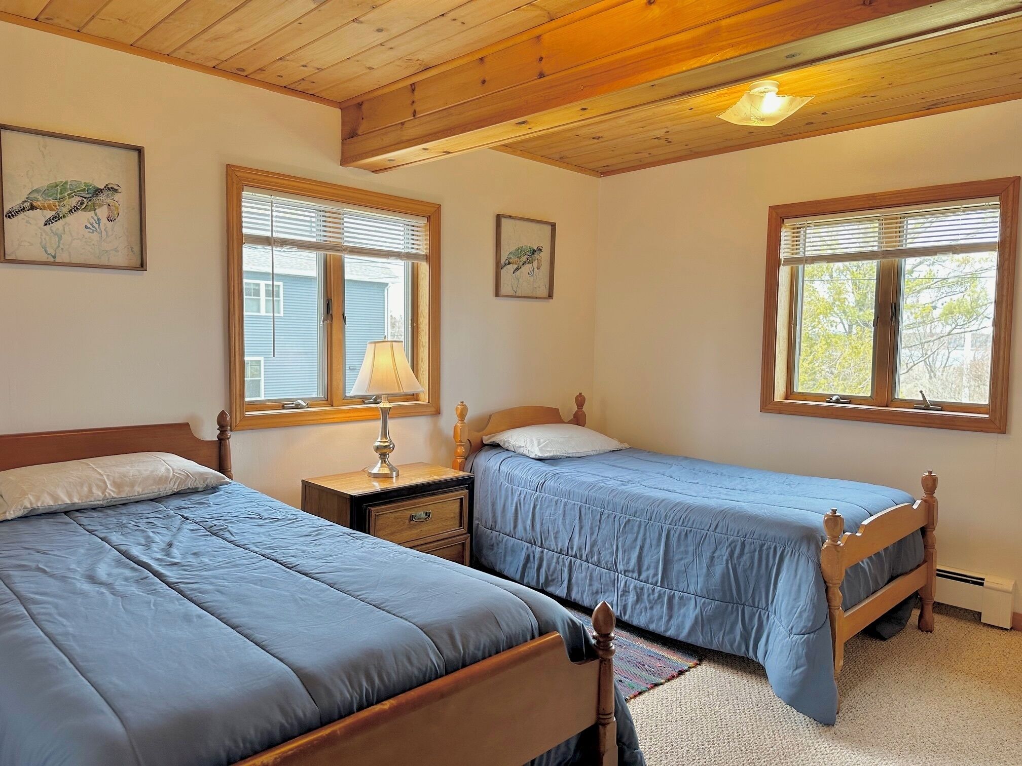 Quarto com duas camas de solteiro, cabeceiras de madeira, mesa de cabeceira com abajur e janelas com persianas.
