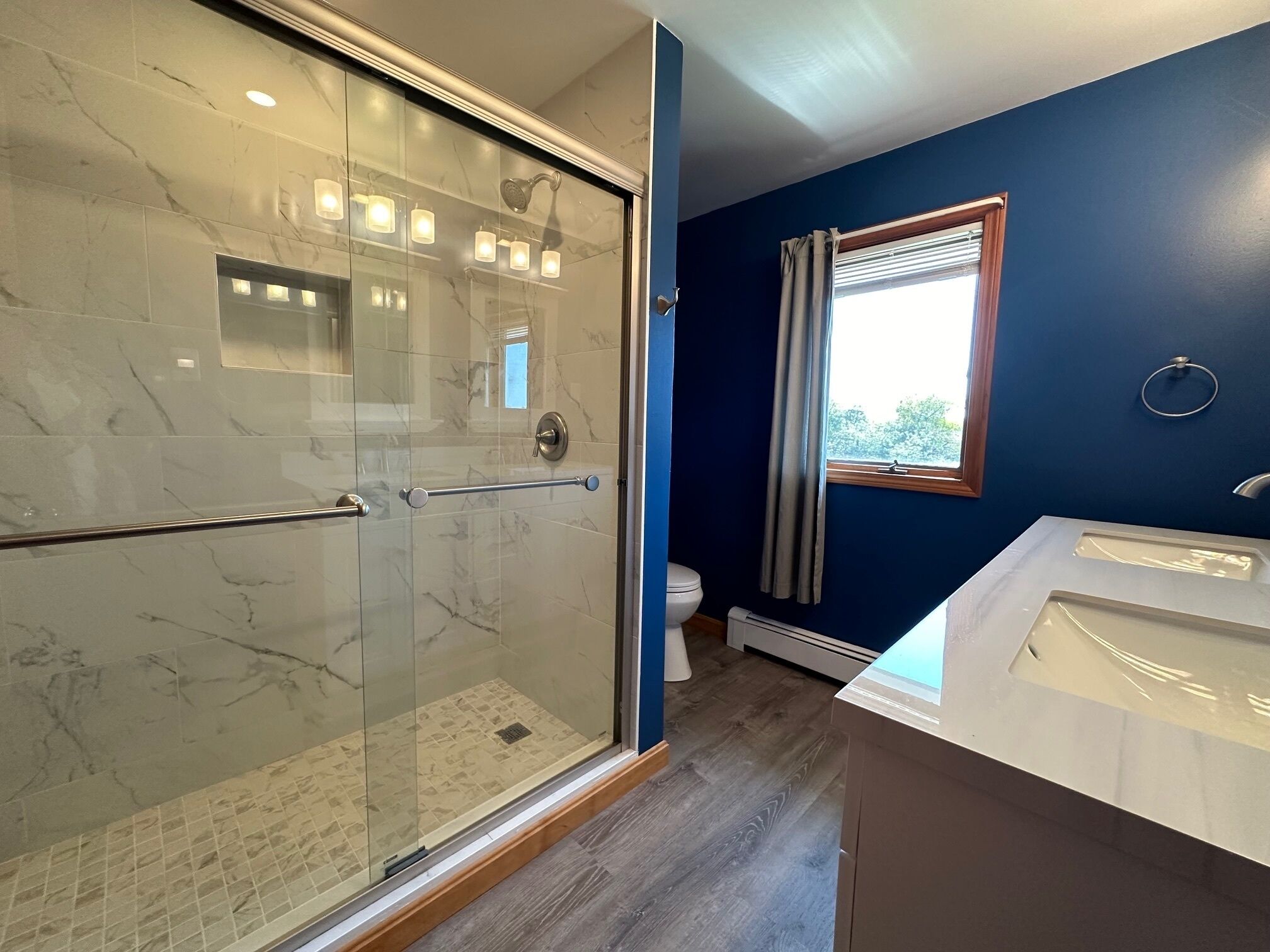 Un bagno con cabina doccia in vetro, un lavandino bianco e una finestra con tende.