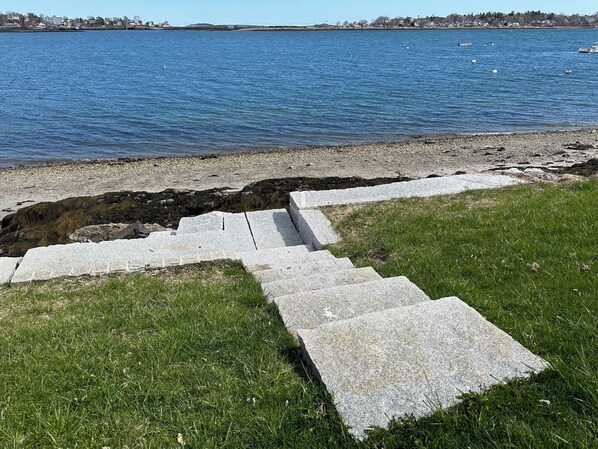 Una escalera de piedra que conduce a una zona con césped junto a un cuerpo de agua.