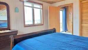 A bedroom with a wooden ceiling, a large bed with a blue mattress, a dresser, a window with blinds, and a door leading outside. - Enjoy Stunning Ocean Views & Coastal Access at Sea Mist Overlook! (Harpswell)
