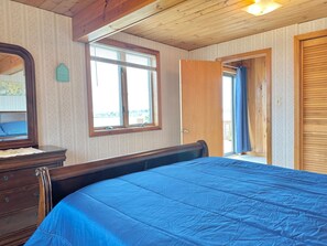 A bedroom with a wooden ceiling, a large bed with a blue mattress, a dresser, a window with blinds, and a door leading outside. - Enjoy Stunning Ocean Views & Coastal Access at Sea Mist Overlook! (Harpswell)