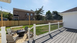 A wooden deck with a white railing, outdoor seating, and a view of a backyard with a wooden fence and a house in the background. - Cozy Dog-Friendly Cape May Escape- Short Walk to Beach (Lower Township)