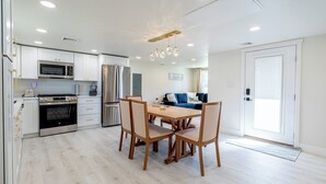 A modern kitchen with white cabinets, stainless steel appliances, and a dining area with wooden chairs and a table. - Cozy Dog-Friendly Cape May Escape- Short Walk to Beach (Lower Township)