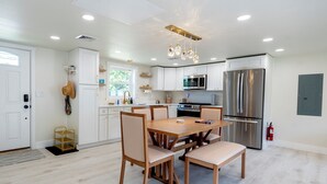 A modern kitchen with white cabinets, a wooden dining table, and stainless steel appliances. - Cozy Dog-Friendly Cape May Escape- Short Walk to Beach (Lower Township)