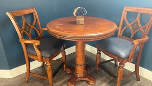 Una mesa redonda de madera con un jarrón de flores, acompañada por dos sillas con asientos acolchados.
