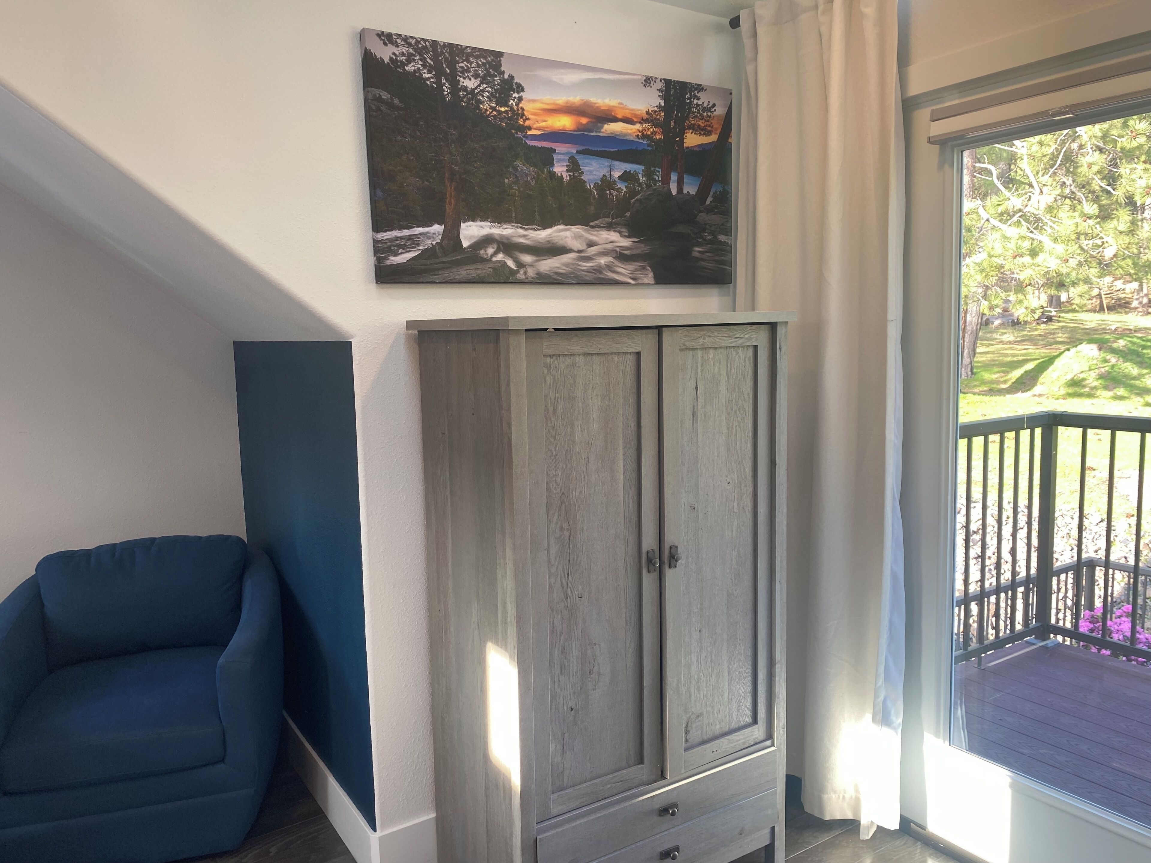 A room with a blue armchair, a grey cabinet, and a painting of a sunset landscape.