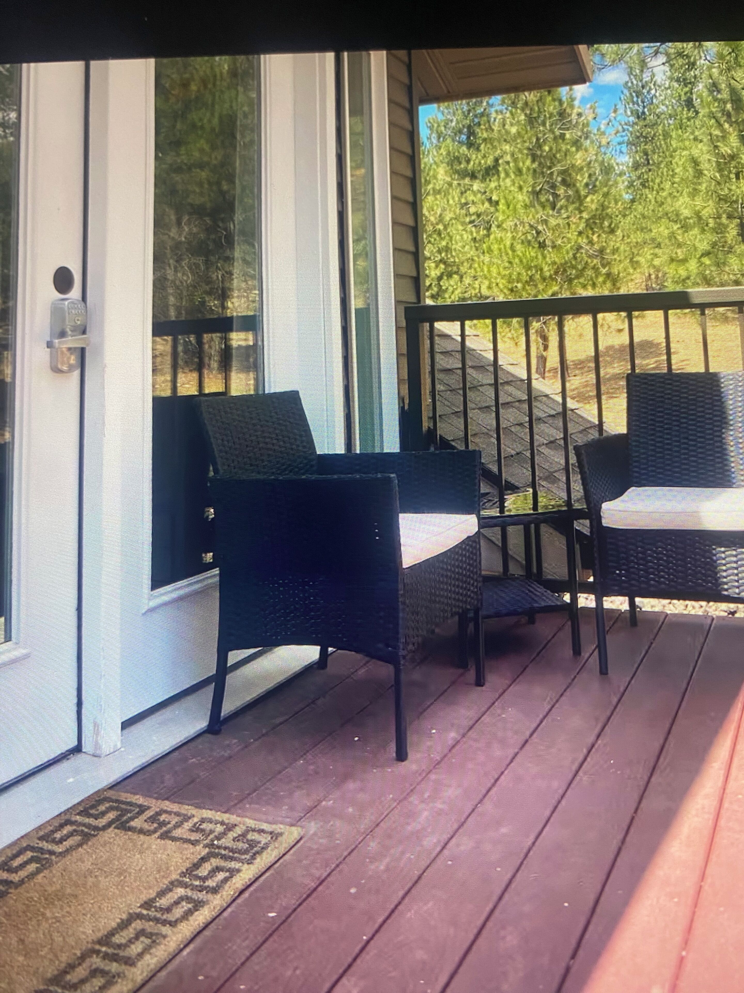 A porch with two wicker chairs, a wooden deck, and a door with a glass panel.