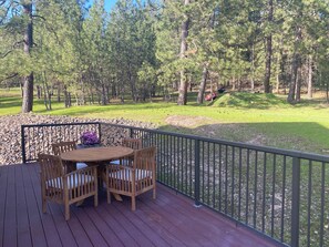 A wooden deck with a table and chairs, surrounded by a metal railing, overlooking a grassy area with trees. - High-end studio on five acre estate with over 100 five star reviews! (Newman lake)