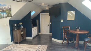 Un dormitorio con cama, una mesa de comedor con sillas, una zona de cocina con armarios y un televisor montado en la pared.
