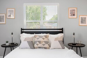 A bedroom with a bed, two bedside tables, a window with blinds, and framed artwork on the walls. - 1.4 Mi to AT&T | Mini Golf + Hoops | Sleeps 12 (Arlington)