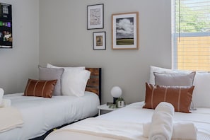 A hotel room with two beds, a TV mounted on the wall, and framed pictures on the wall.