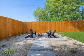 A backyard with a wooden fence, two Adirondack chairs, a fire pit, and a well-maintained lawn. - Sleeps 12 | Pickleball + Mini Golf + Pool Table (Arlington)
