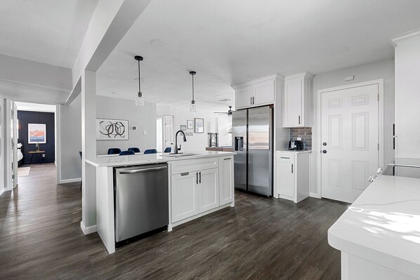 A modern kitchen with white cabinetry, stainless steel appliances, and a wooden floor.