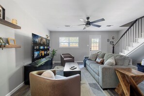 A modern living room with a grey sofa, a brown armchair, a coffee table, a TV on a stand, and a ceiling fan.