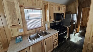 A compact kitchen with wooden cabinets, a sink, a stove, and a microwave. - Relax in the Fox Den | Private 2BR Cabin Close to Beach & Activities (Isle)