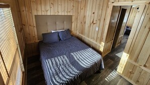 A bedroom with a wooden slat ceiling, a bed with a patterned bedspread, and a wooden door. - Relax in the Fox Den | Private 2BR Cabin Close to Beach & Activities (Isle)