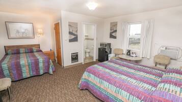 A hotel room with two beds, a desk, a chair, a microwave, a refrigerator, and a window with curtains.