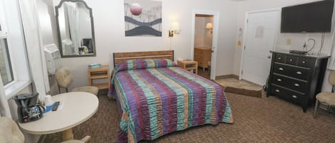 Ein Hotelzimmer mit Bett, Schreibtisch, Stuhl, Kommode, Fernseher und einem Fenster mit Vorhängen.