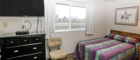 A hotel room with a bed, a dresser, a chair, a television, and a window with curtains.