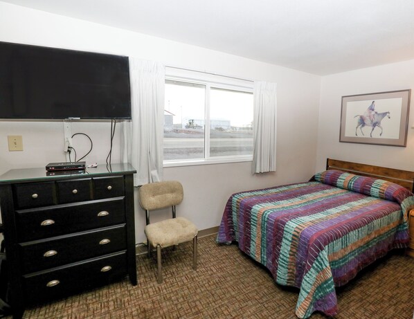 A hotel room with a bed, a dresser, a chair, a television, and a window with curtains. - Condon Motel (Condon)