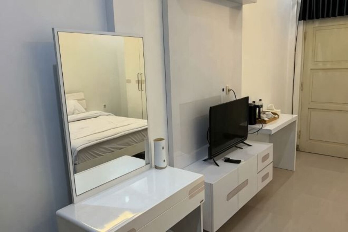 A modern hotel room with a large mirror, a flat-screen TV, a white dresser, and a door.