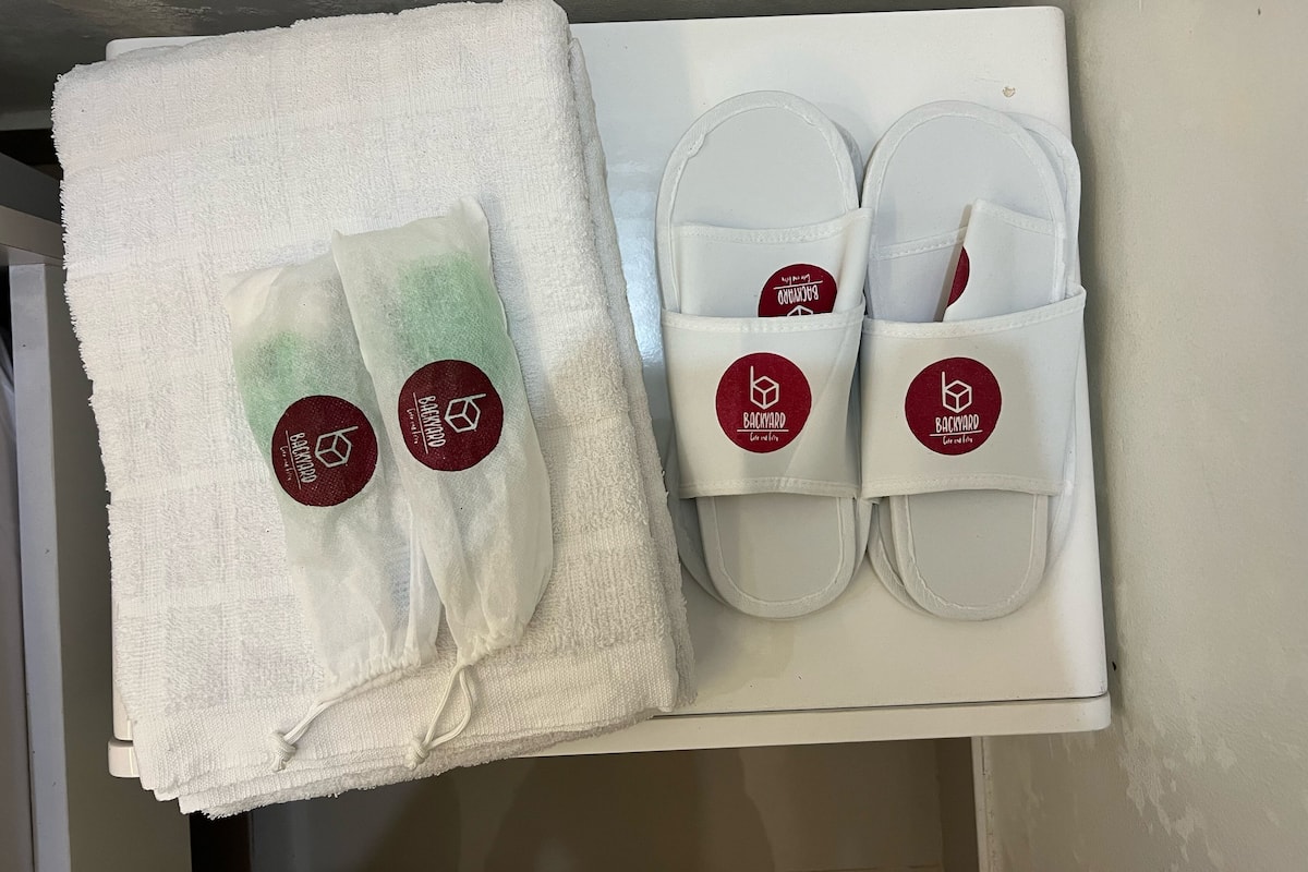 A box containing a white towel, a pair of white slippers, and a white bath mat.