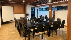Ein Konferenzraum mit großem Tisch, mehreren Stühlen, einer Projektionsleinwand und einer Whiteboard-Wand.