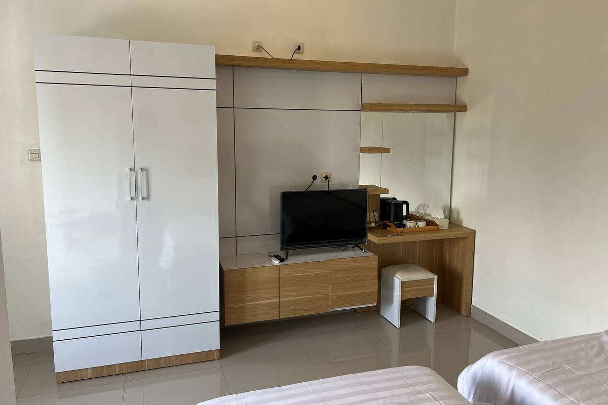 A bedroom with a bed, a desk with a TV, a small stool, and a wardrobe.