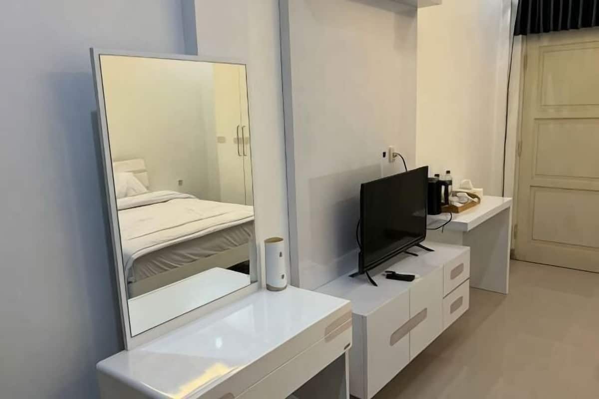 A modern hotel room with a large mirror, a flat-screen TV, a white dresser, and a door.
