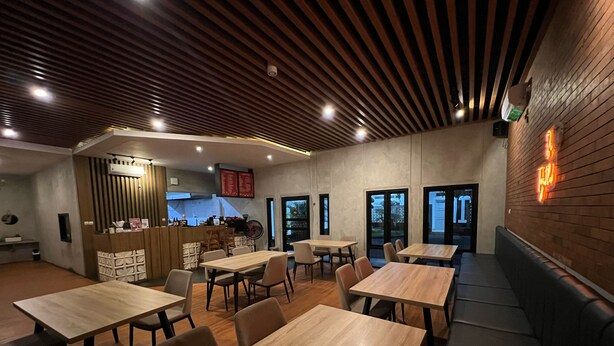 Ein Restaurantinneres mit Holztischen und -bänken, einer Theke mit Speisekarte und Blick durch die Glastüren.