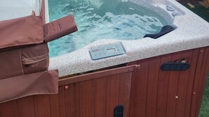 Un bain à remous doté d’un panneau de commande, entouré d’une clôture en bois et avec un bâtiment visible en arrière-plan.