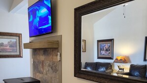 Un salon doté d’une cheminée en pierre, d’un meuble de télévision noir, d’un pouf en cuir, d’un grand miroir et d’un téléviseur fixé au-dessus de la cheminée.