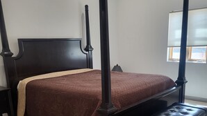 Un lit à baldaquin avec une tête de lit et un pied de lit sombres, une couvre-lit marron et un banc assorti placé au pied du lit.